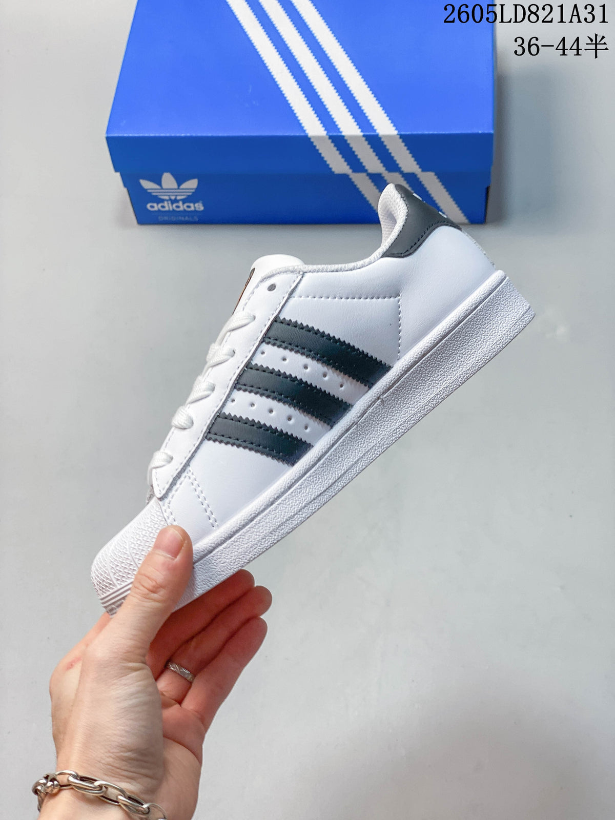 Side view of a white Adidas Superstar sneaker with dark stripes and a shell toe.