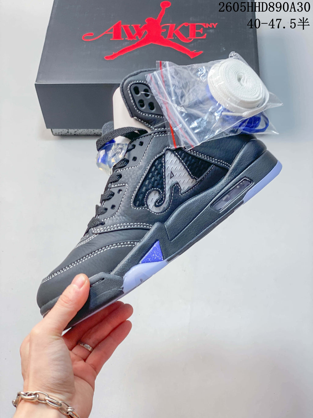Side view of a gray Air Jordan 5 sneaker with blue accents and an extra lace bag