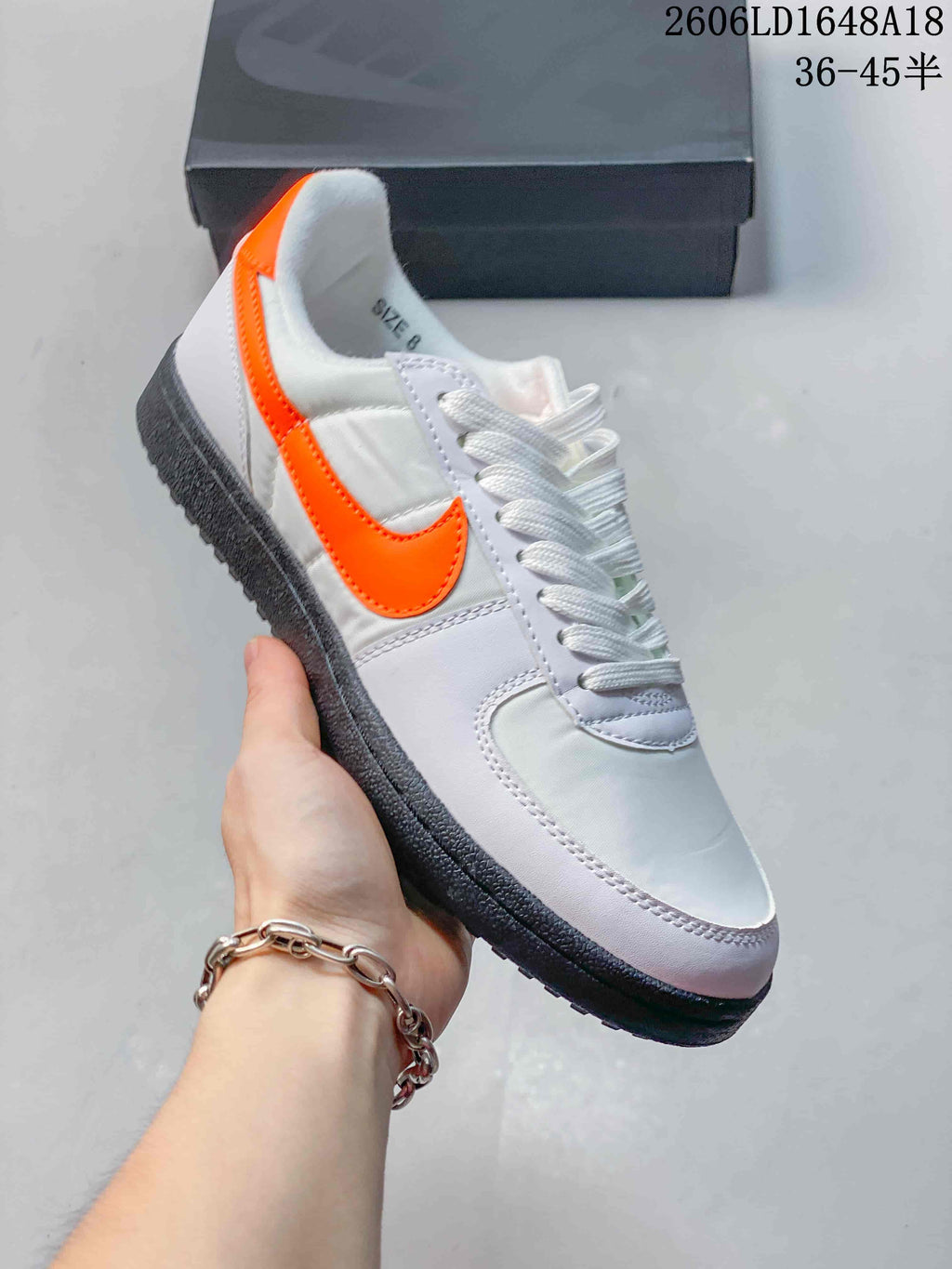 Angled view of the white low-top sneaker with orange Swoosh and dark outsole
