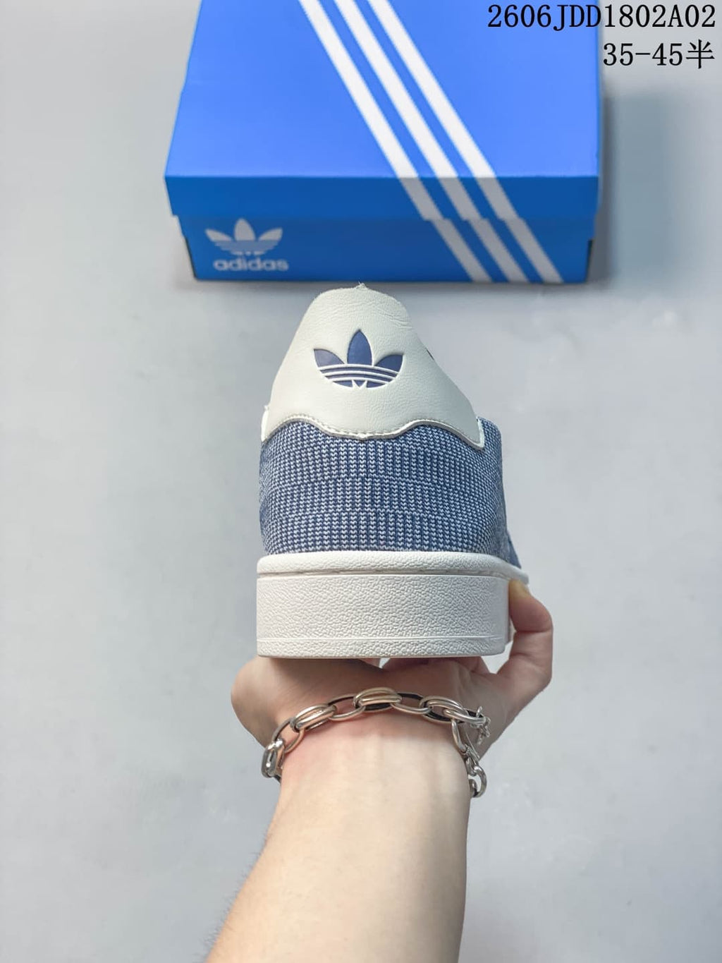 Rear view of the blue and white sneaker showing the white heel tab, blue textile-look upper, Trefoil logo, and flat white sole.