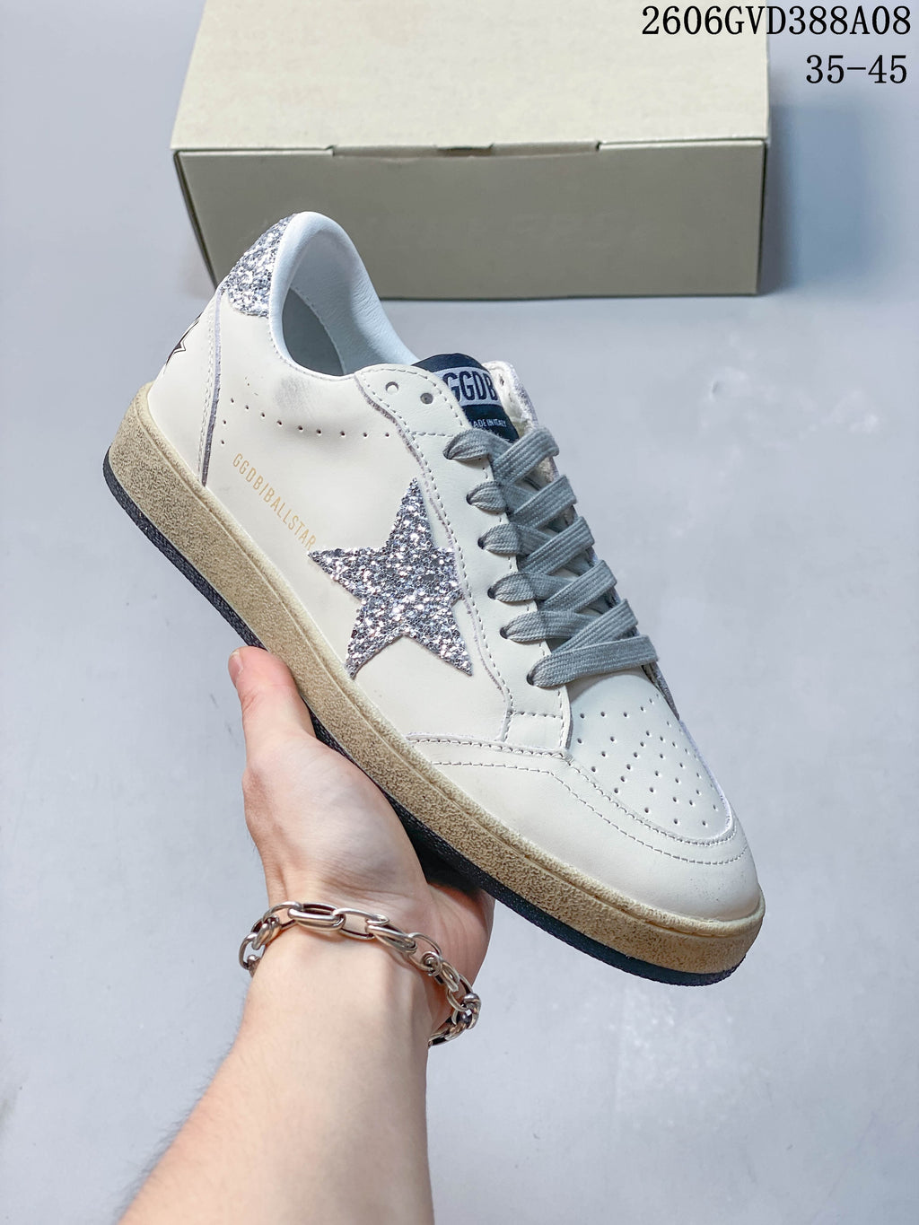 Side view of white sneaker with silver glitter star, gray laces, and beige midsole