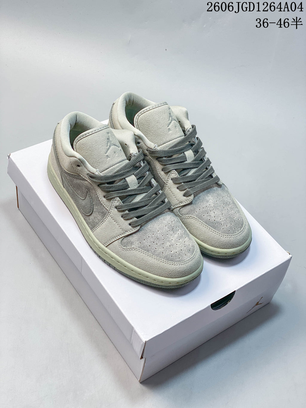 Pair of pale gray Air Jordan 1 Low sneakers with darker gray laces on a white box
