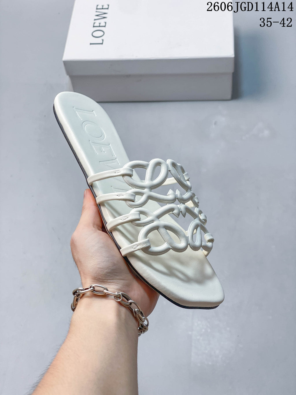 Angled view of a white flat slide sandal with raised Anagram-style straps