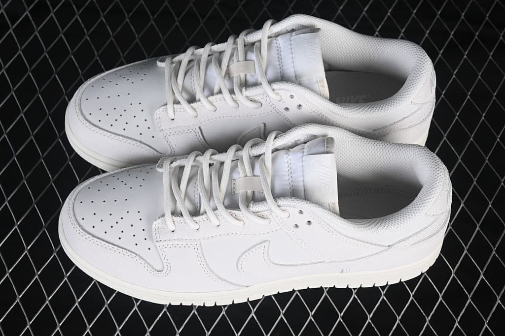 Pair of white Nike SB Dunk Low sneakers shown from above, with perforated toes and tonal side Swooshes.