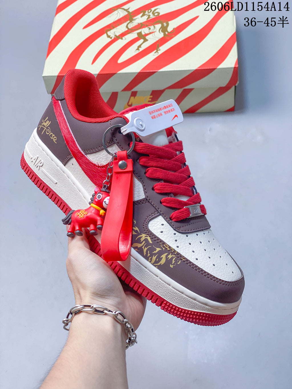 White, brown and red low-top sneaker with patterned overlays, red laces and a hanging charm