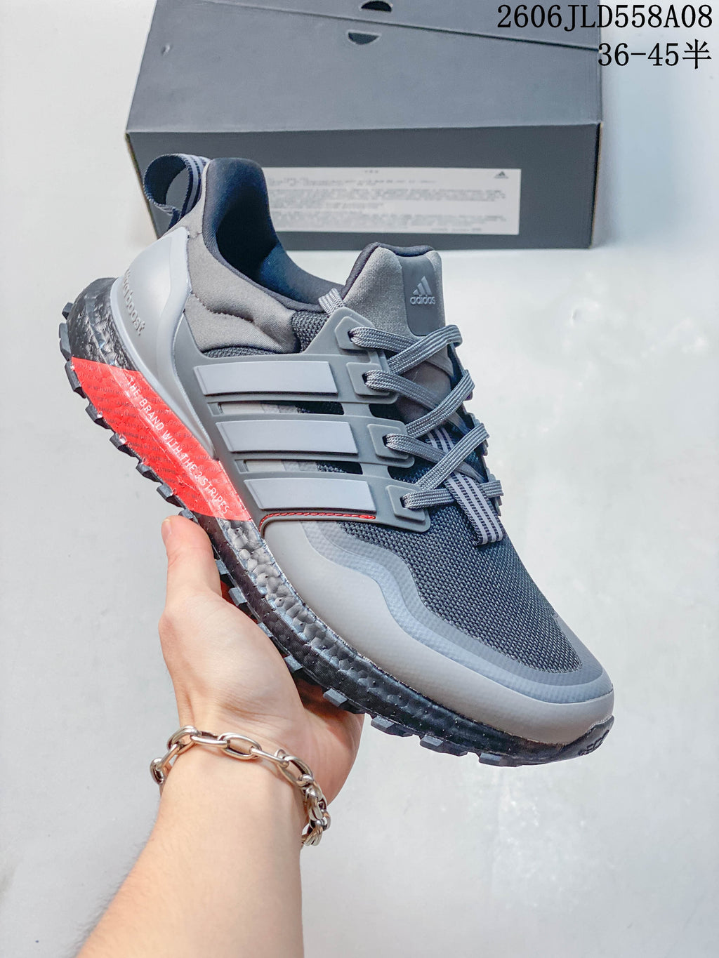 Angled side view of the grey sneaker showing adidas branding, red accents and the treaded outsole.