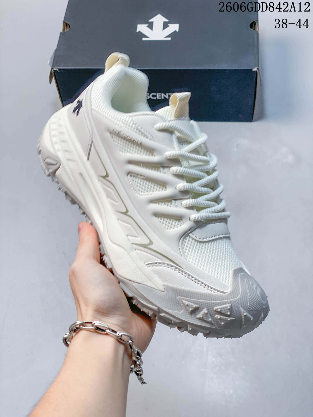 Angled view of the white DESCENTE sneaker showing its mesh-style panels, laces and chunky sole; the image displays size range 38–44.
