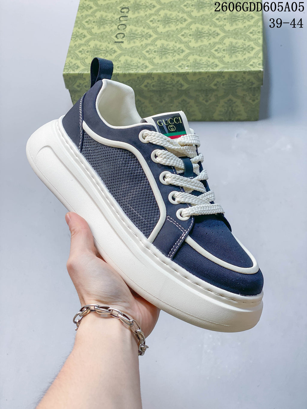 Side view of a navy lace-up sneaker showing textured panels, contrast piping and a thick white sole.