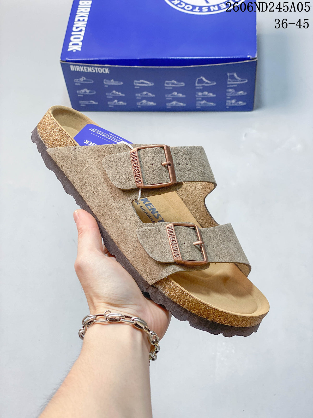Beige-gray two-strap sandal with copper-tone buckle details.