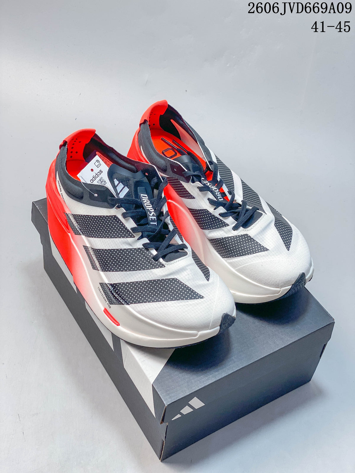 Pair of white adidas Adizero Dropset Elite shoes with dark detailing and bright red heels, displayed on a box
