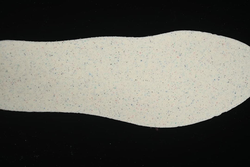 Light-colored sneaker insole shown from above, with small multicolor flecks.