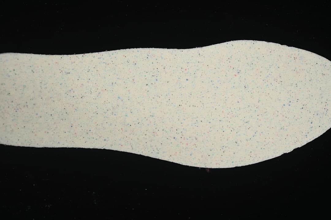 Light-colored sneaker insole shown from above, with small multicolor flecks.