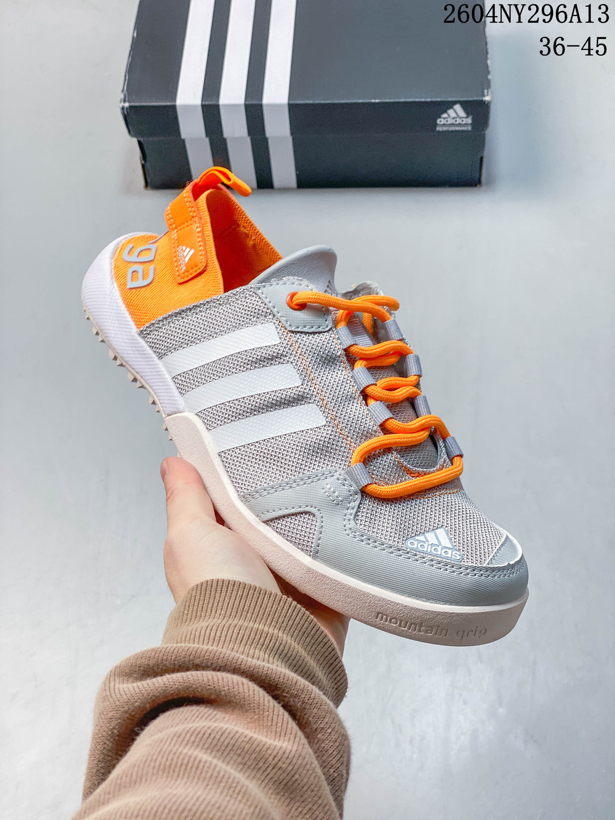 Angled side view of the grey shoe with white stripes, orange accents and patterned outsole.
