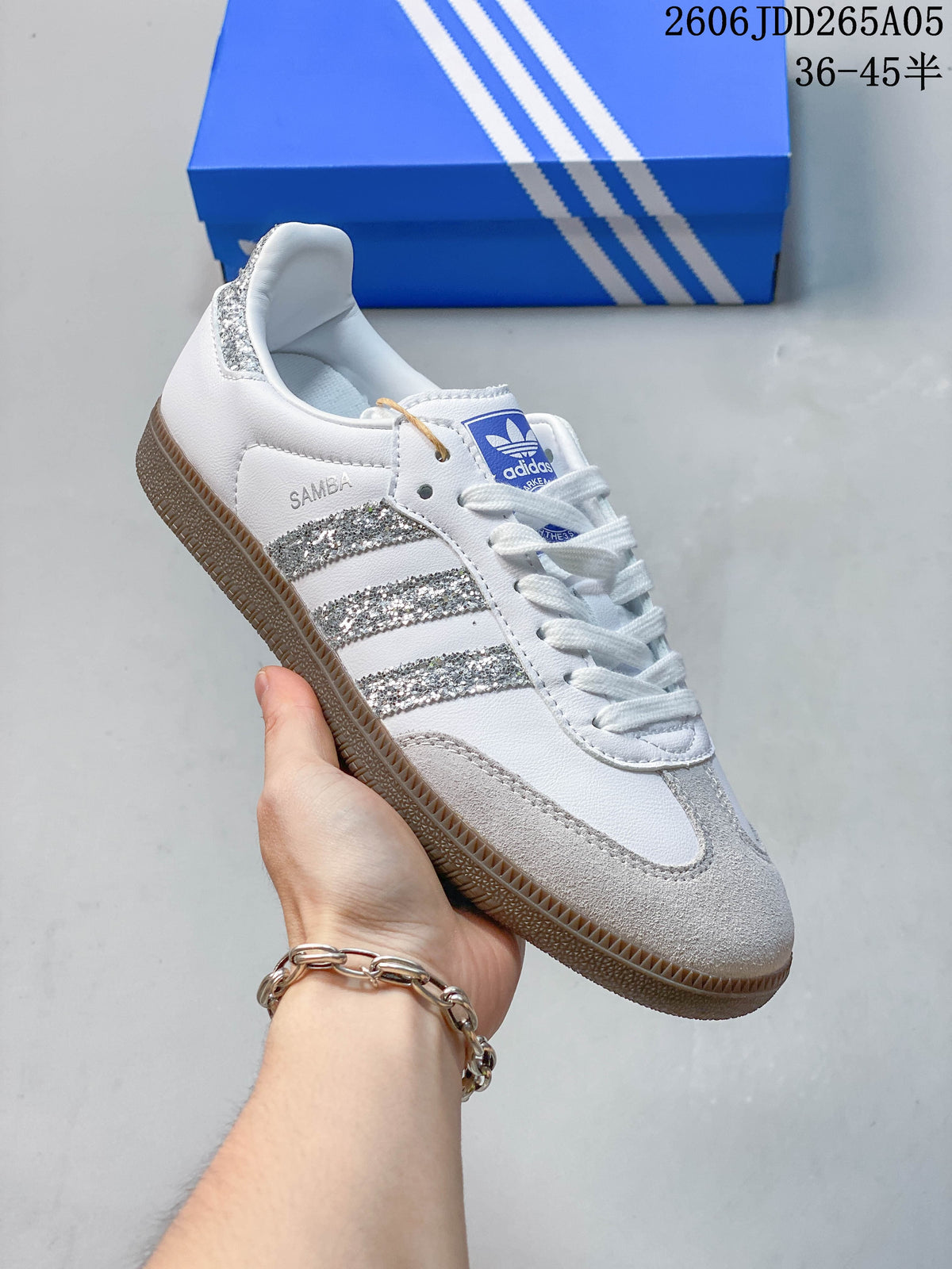 Side view of a white adidas Samba OG sneaker with silver glitter stripes, pale gray overlays, and a gum-colored outsole.