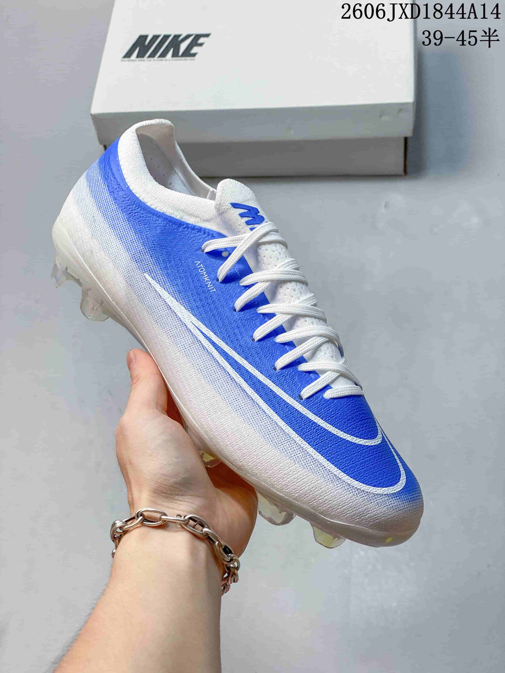 Angled side view of a blue-and-white Nike soccer cleat with Swoosh detailing.