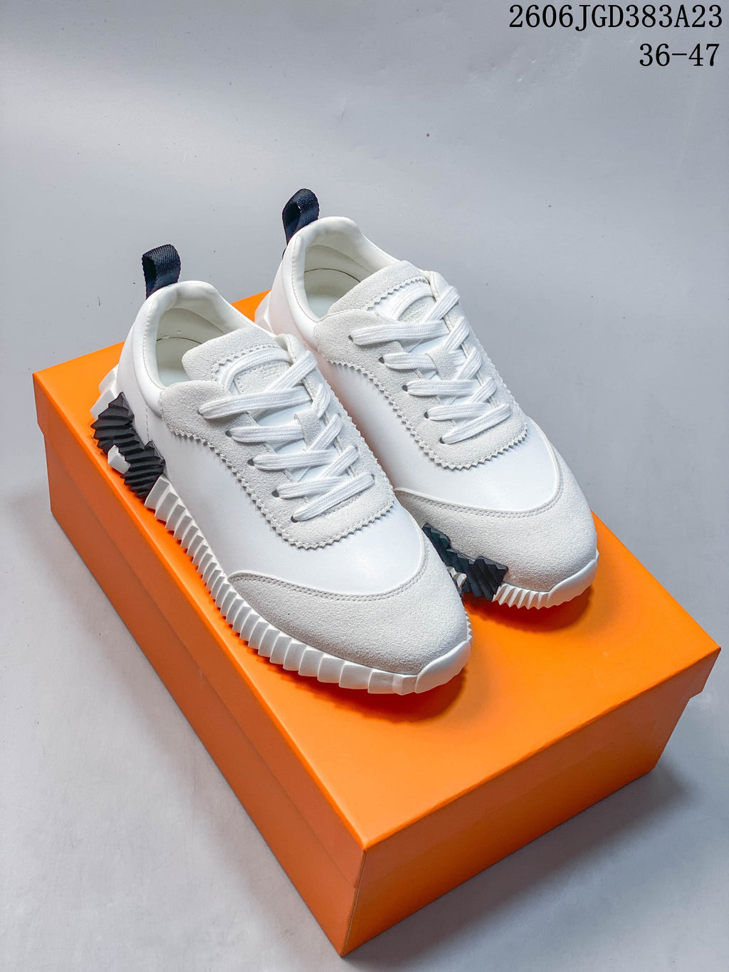 Pair of white low-top lace-up sneakers with gray textured overlays and ridged soles, shown on an orange box.