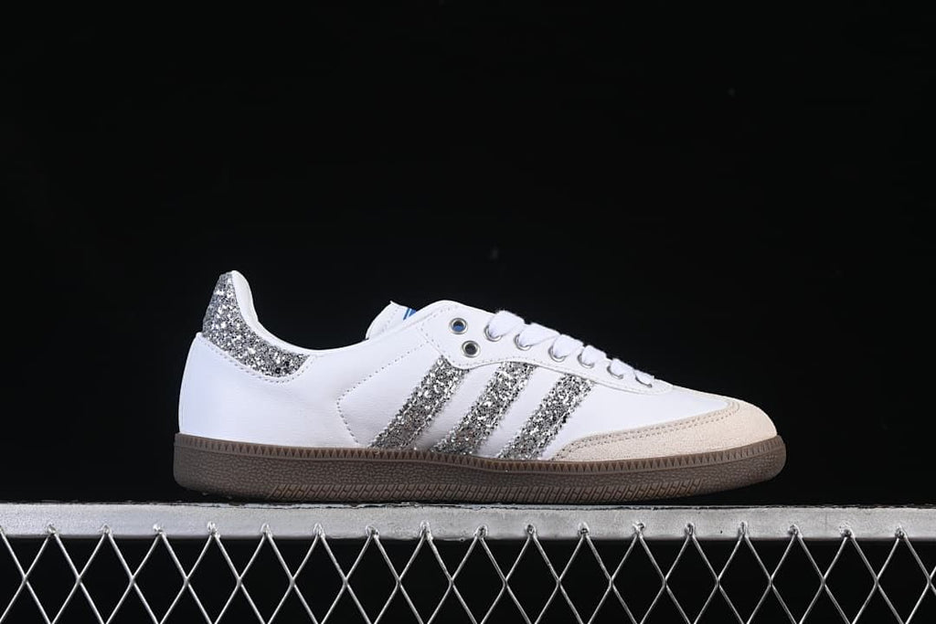 Side profile of a white sneaker with silver glitter-effect stripes and heel accent.