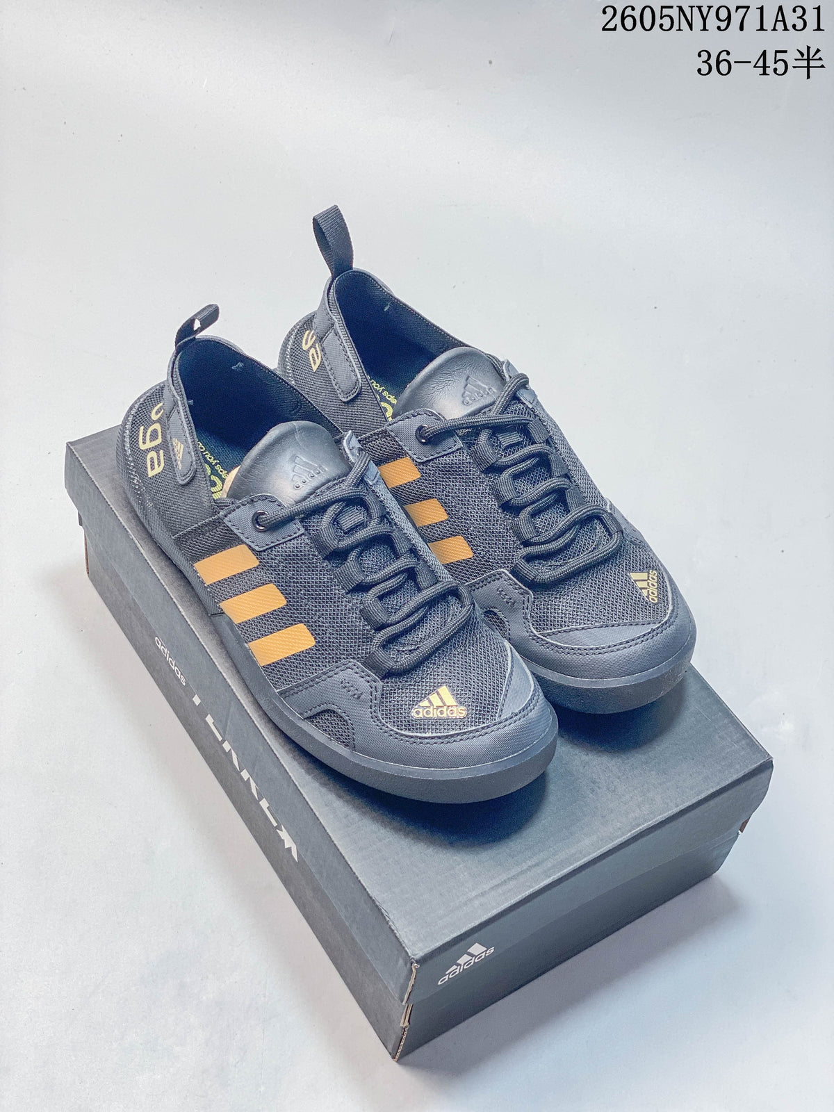 Pair of dark gray adidas Terrex outdoor shoes with yellow-orange stripes, shown on a shoebox