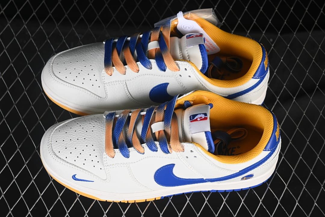 Top view of a pair of white Nike SB Dunk Low sneakers with blue and gold-toned details and mixed-color laces.