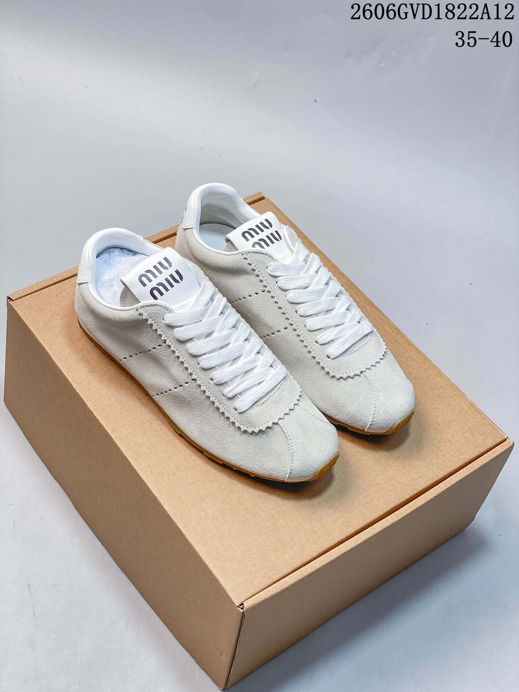 Pair of white and light gray Miu Miu low-top lace-up sneakers with perforated sides and star-pattern outsole, shown on a box.