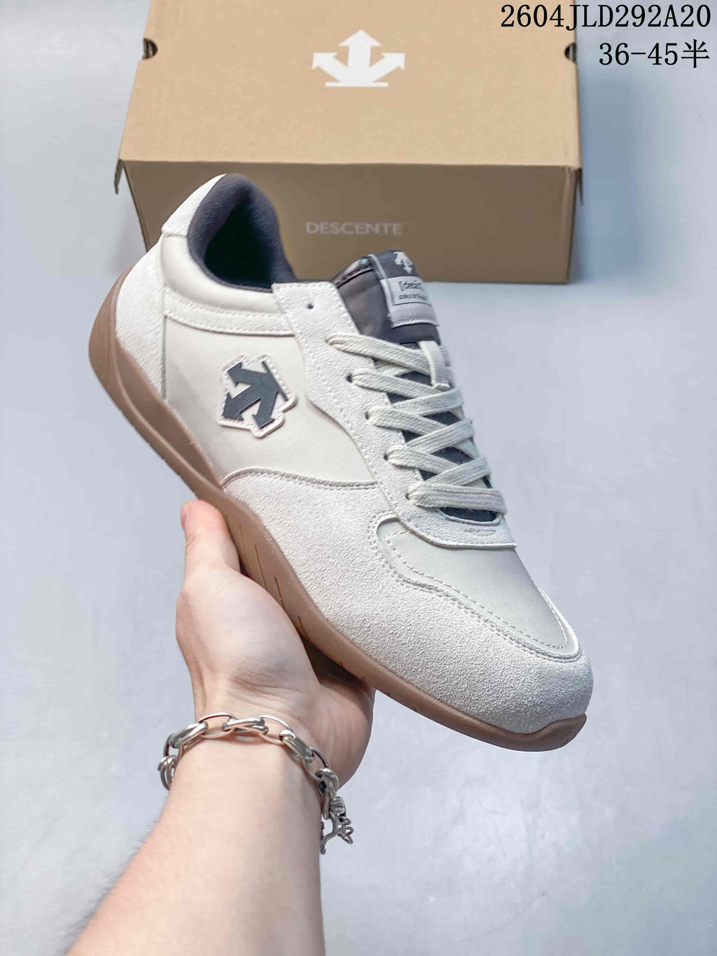 Side view of a white and gray Descente sneaker with a gum-tone outsole and contrasting panel details.