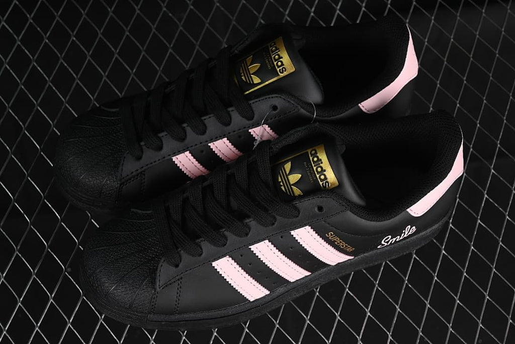 Pair of black Adidas Superstar sneakers with pink stripes, shown from above