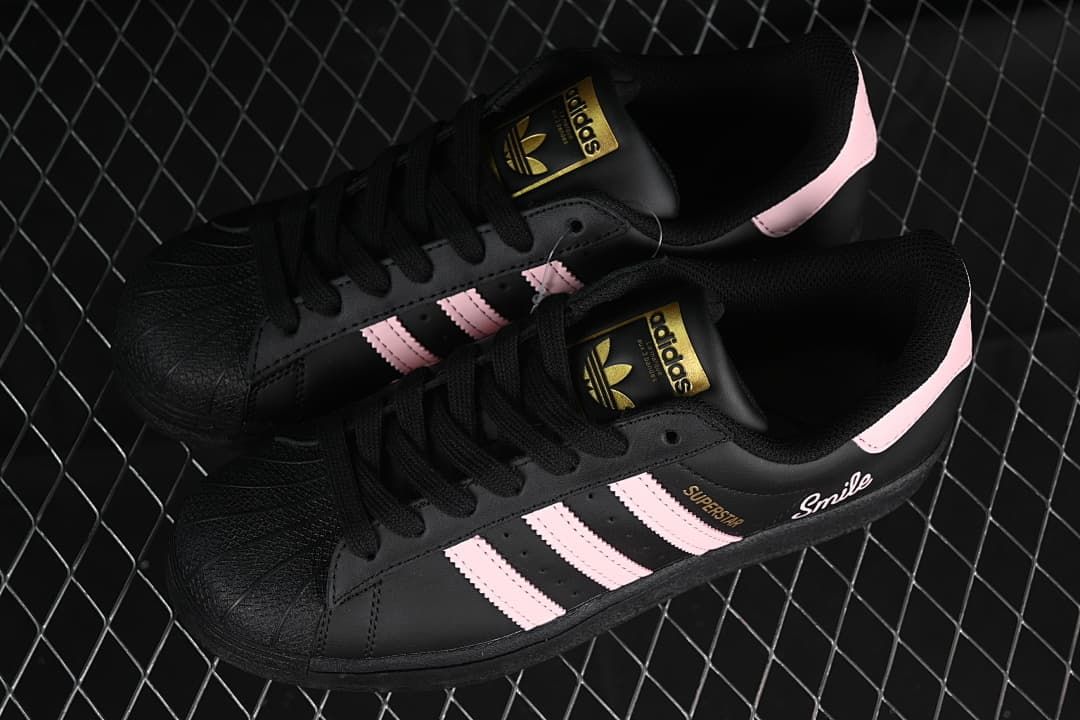 Pair of black Adidas Superstar sneakers with pink stripes, shown from above