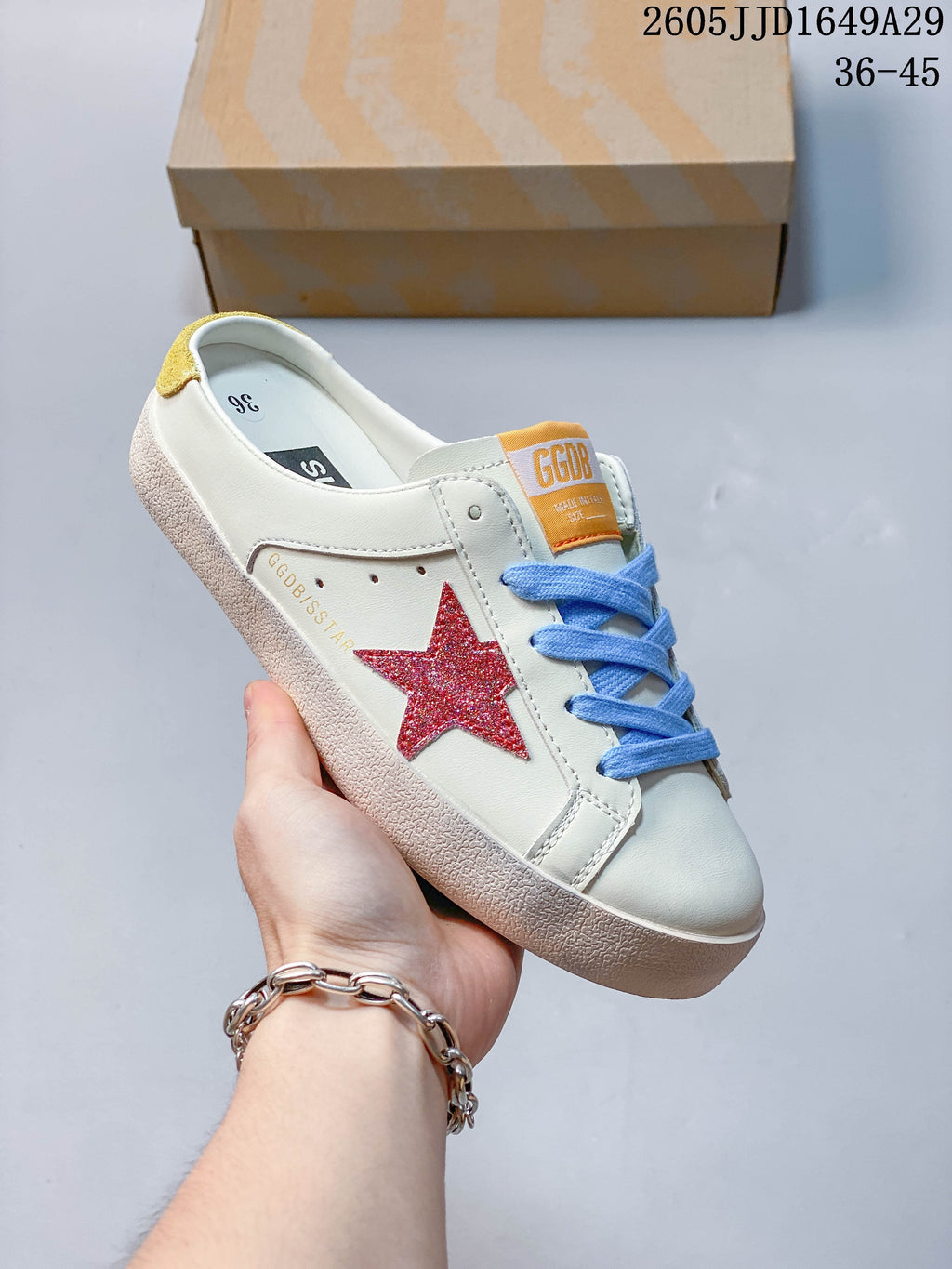Angled view of a white sneaker with a red glitter star, blue laces, and yellow heel detail
