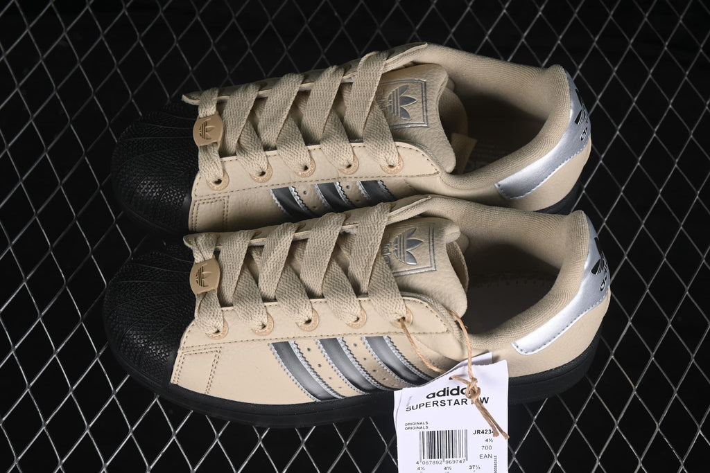 Top view of the pair showing the beige uppers, laces, black shell toes, silver heel panels, and product hang tag.