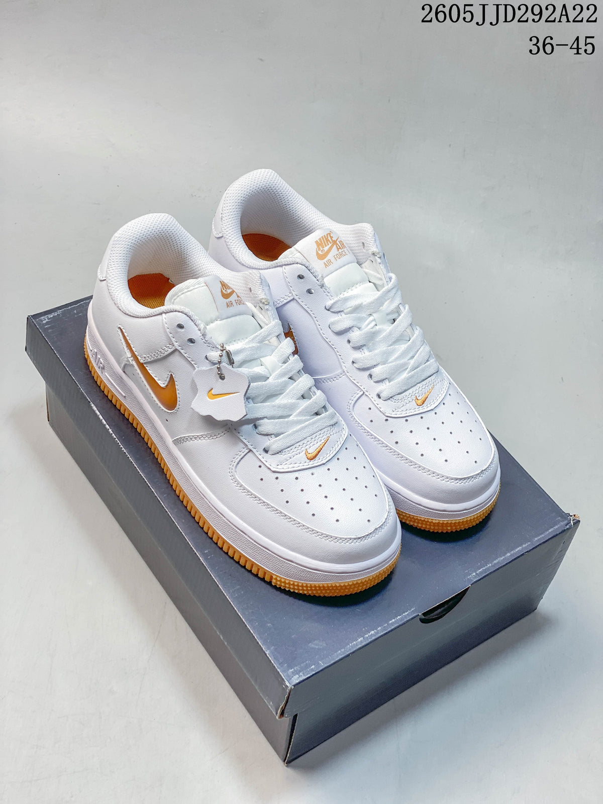 Pair of white Nike Air Force 1 Shadow sneakers with orange-gold details on a shoebox