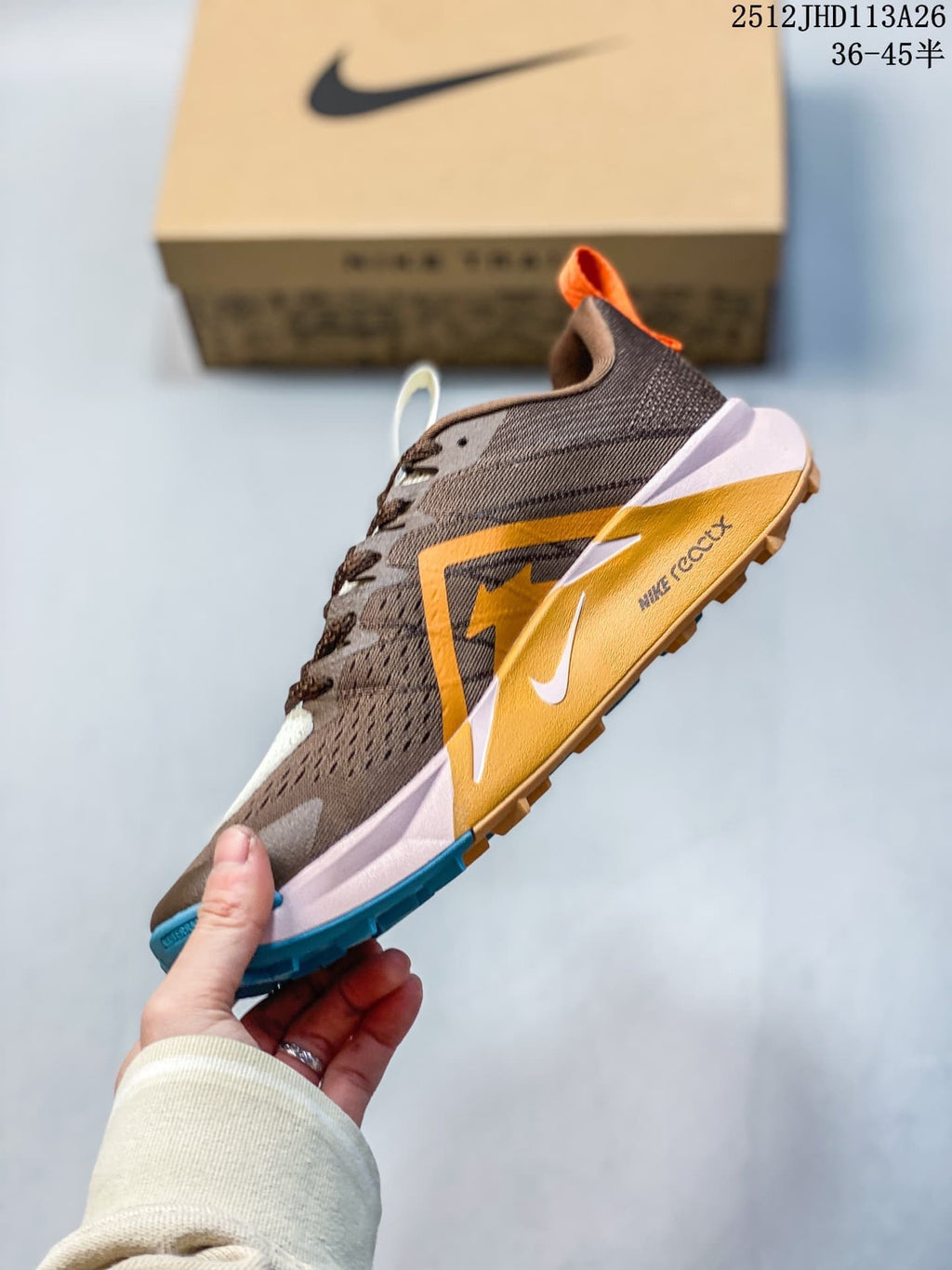 Side view of the Nike ReactX Wildhorse 10 with brown upper, orange overlays, pale pink midsole, and blue outsole details.
