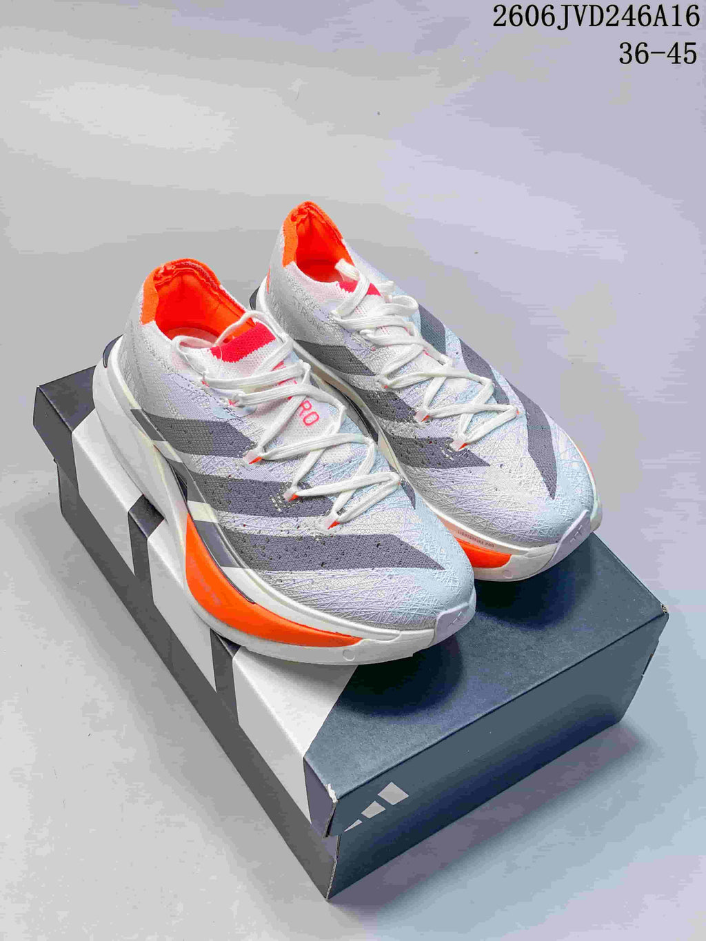 Pair of gray and white Adidas Adizero running shoes with dark stripes and orange accents, shown on a shoe box.