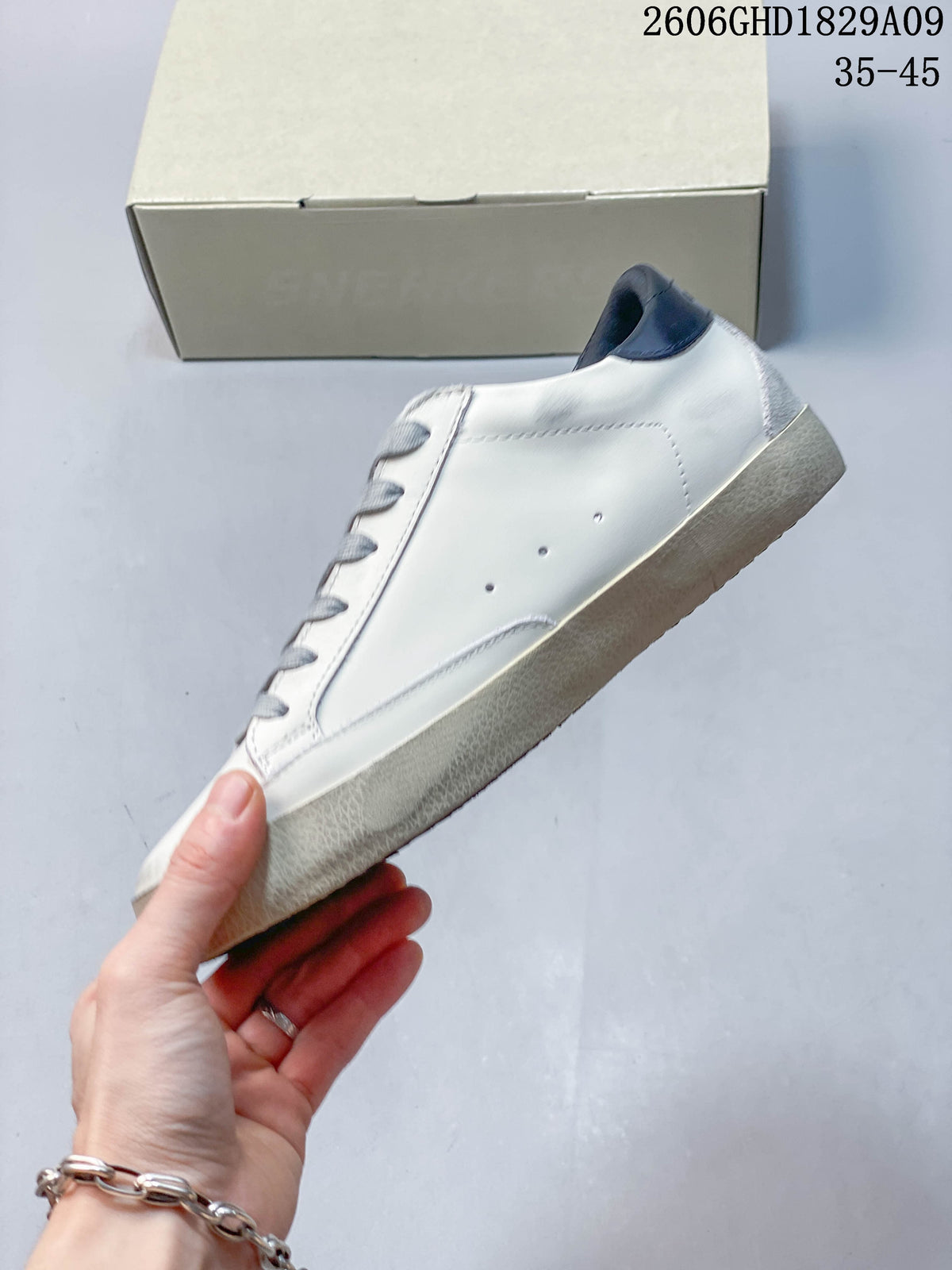 Side view of white low-top sneaker with a dark blue heel tab and textured off-white sole