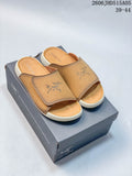 Tan open-toe slide sandals with a wide stitched strap, shown on a branded box.