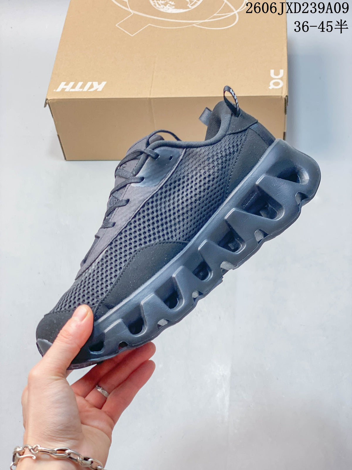 Side view of a charcoal shoe with an open-knit upper and segmented sole.