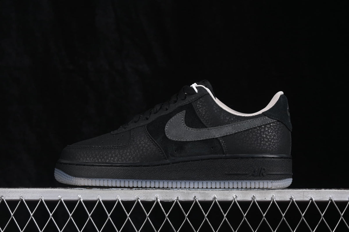 Side profile of black Nike Air Force 1 '07 Low sneakers with dark grey Swoosh accents and a translucent-looking outsole.