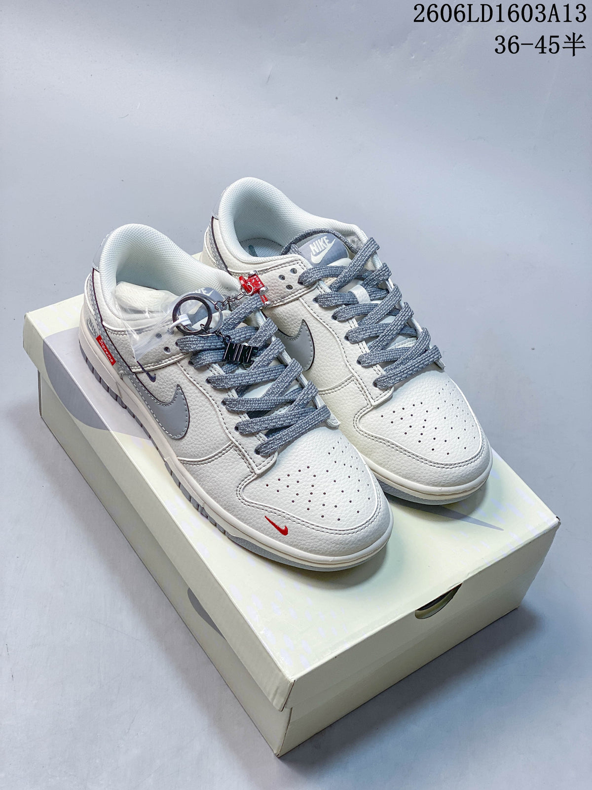 Pair of cream and grey Nike Dunk Low-style sneakers with grey laces and red accents