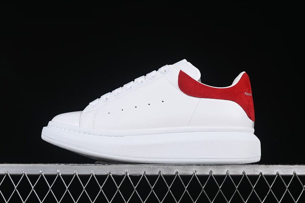 Side view of a white low-top sneaker with a red heel panel and thick white sole.