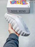 White Nike Mind slide held above its box, showing the textured upper, covered toe, and sculpted outsole.