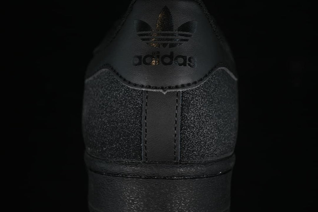 Rear view of the black sneaker with Trefoil branding and speckled heel panels