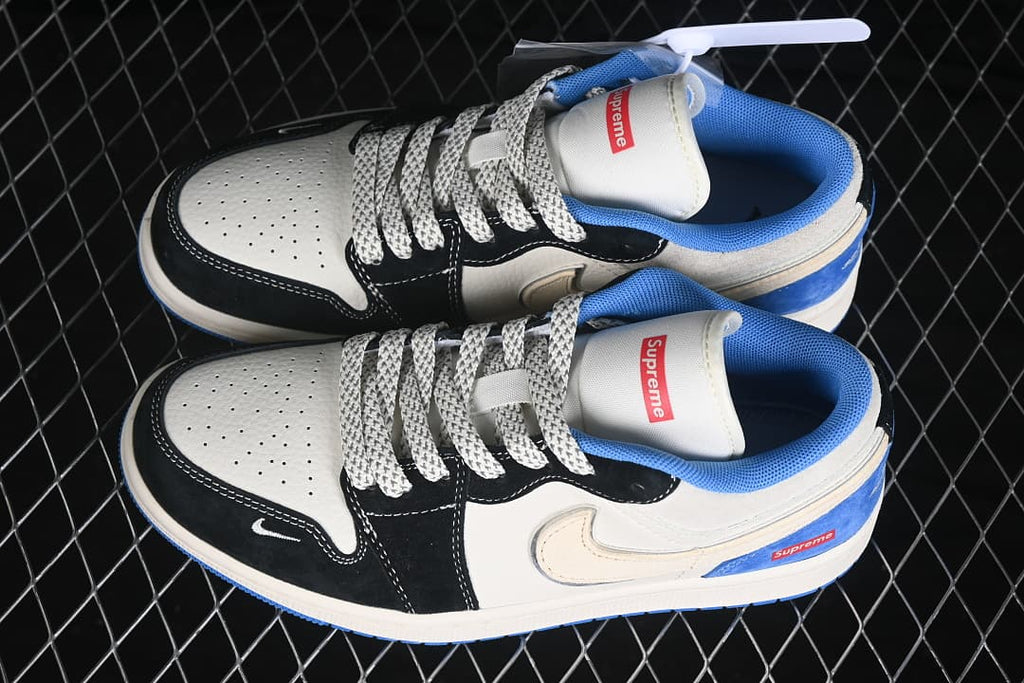 Pair of white, black, and blue Air Jordan 1 Low sneakers with patterned laces and visible Supreme tongue branding.