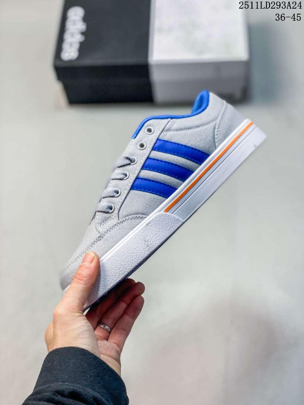Side profile of a gray low-top sneaker with blue stripes and orange sole trim