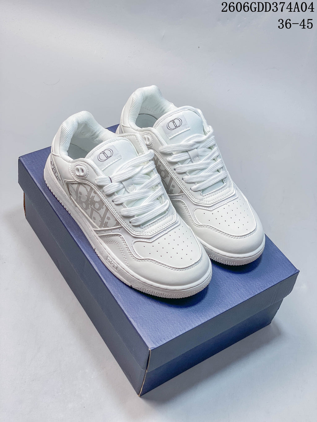 Pair of white Dior low-top sneakers shown from above at an angle, with patterned side panels and a blue shoe box.