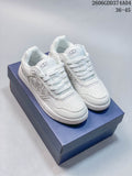 Pair of white Dior low-top sneakers shown from above at an angle, with patterned side panels and a blue shoe box.