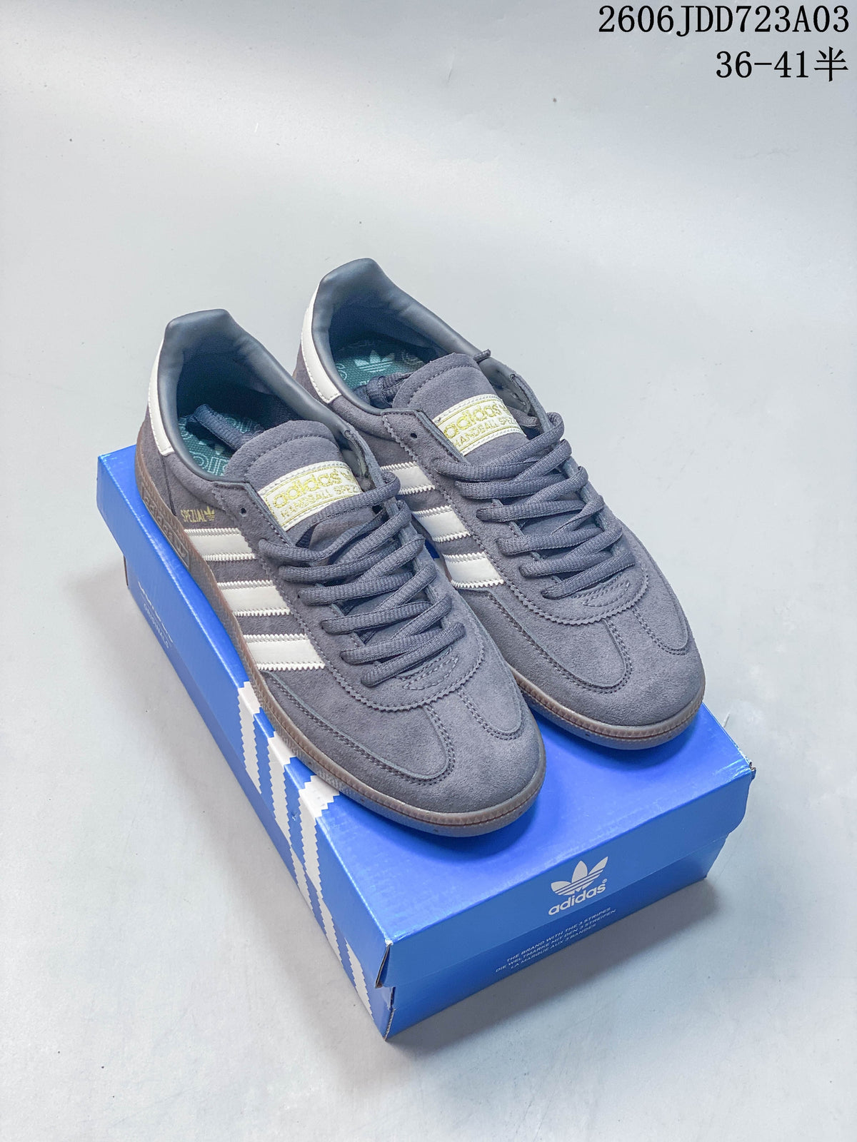 Slate gray Adidas Handball Spezial sneakers with pale stripes and dark laces, shown on a blue shoe box.