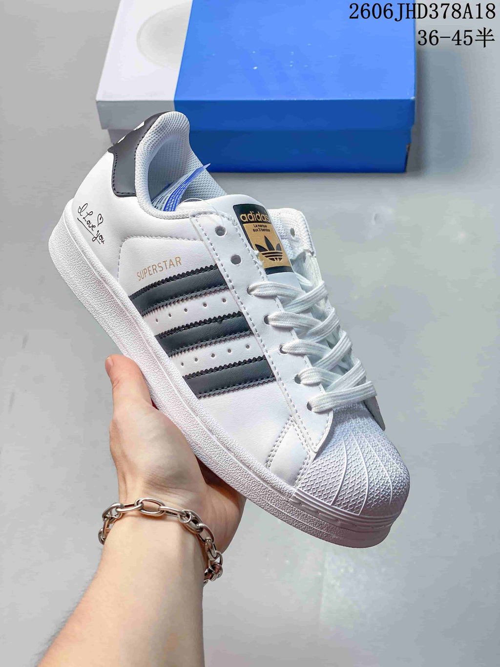 White Adidas Originals Superstar low-top sneaker with dark stripes, textured shell toe, and heel graphics