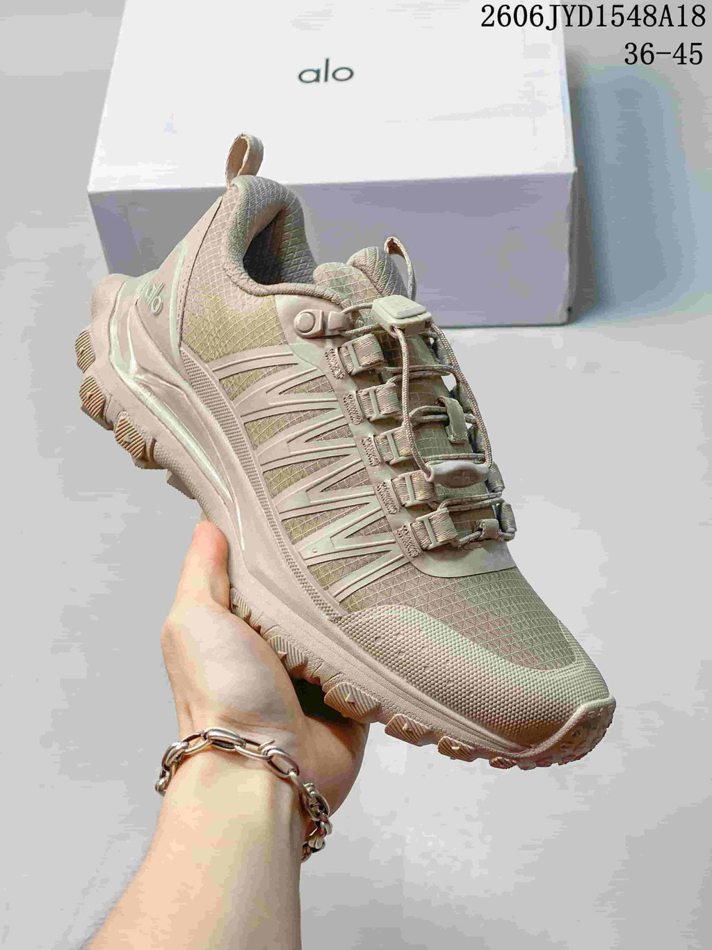Angled side view of a taupe Alo Yoga Trail shoe with its quick-lace system.