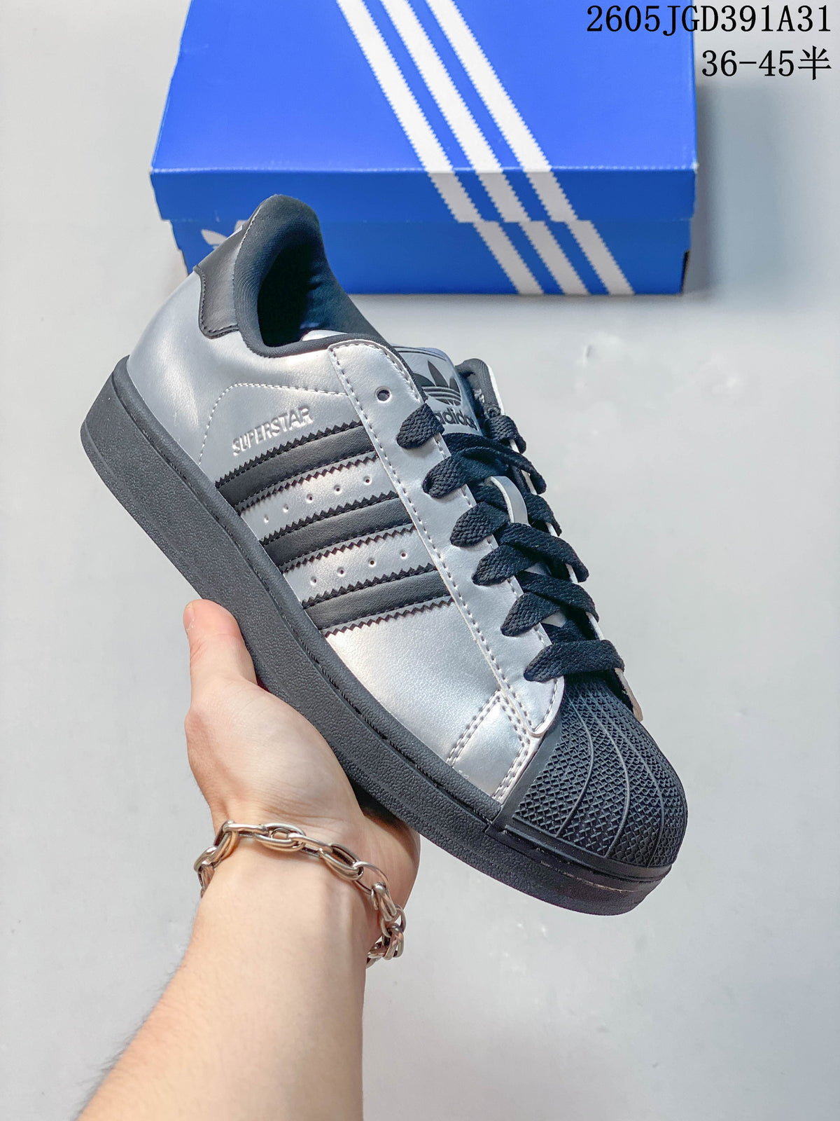 Angled side view of a silver Superstar sneaker with dark three-stripe detailing.
