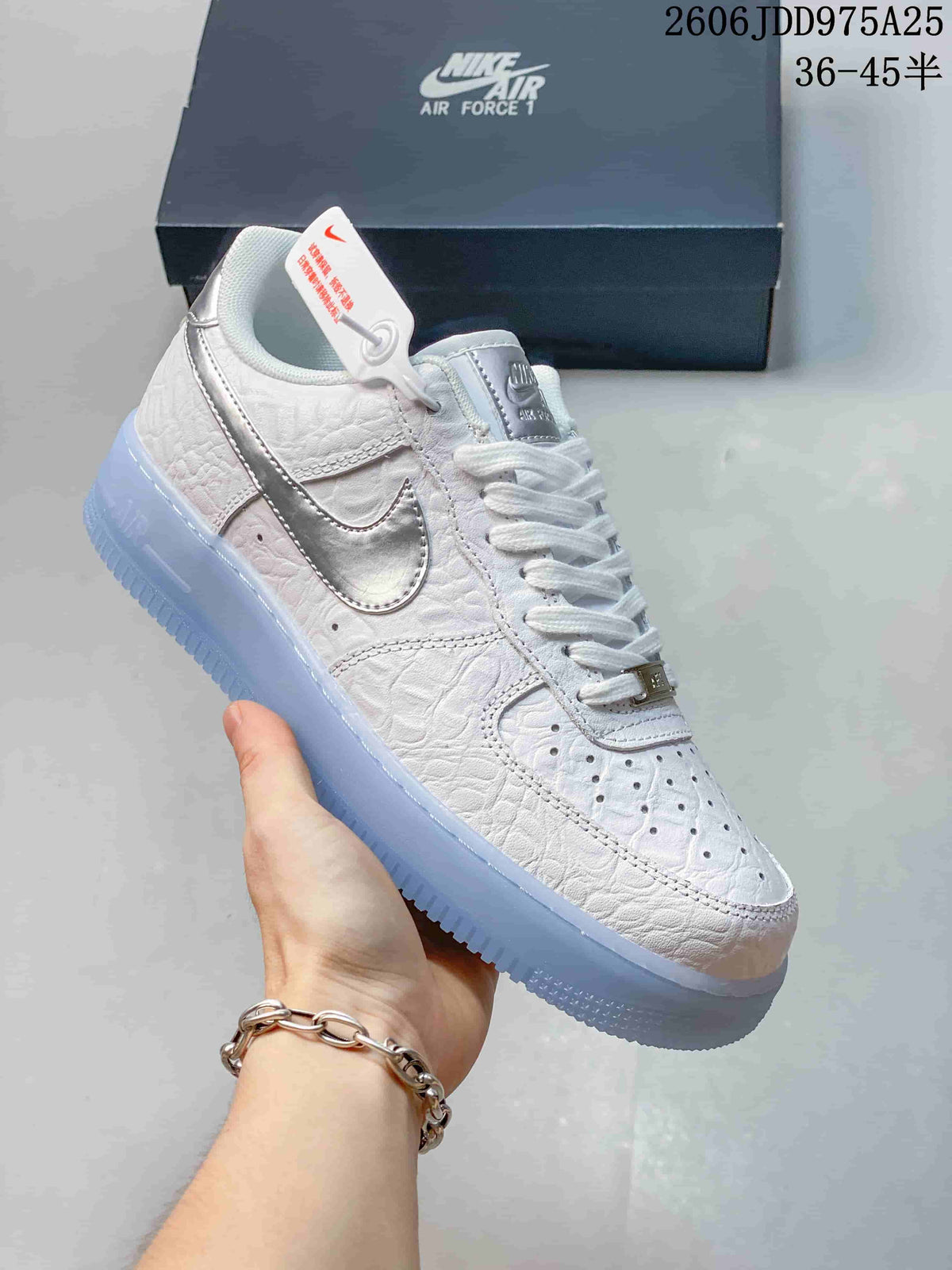 White Nike Air Force 1 low-top sneaker with silver accents and a pale blue outsole, held in front of its box.
