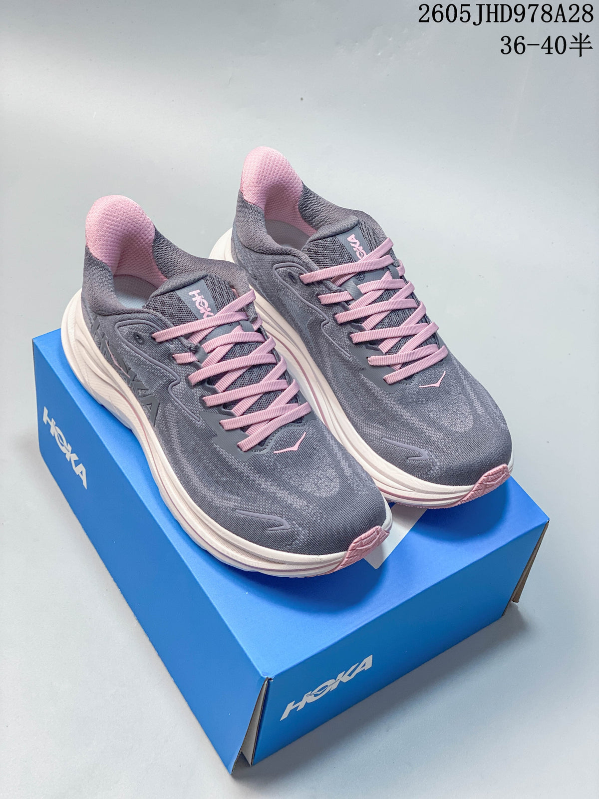 Pair of gray HOKA Clifton 10 running shoes with pink laces and accents on a blue shoe box